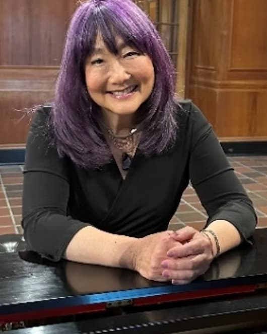 Julie Nishimura, leaning on the lid of a grand piano.