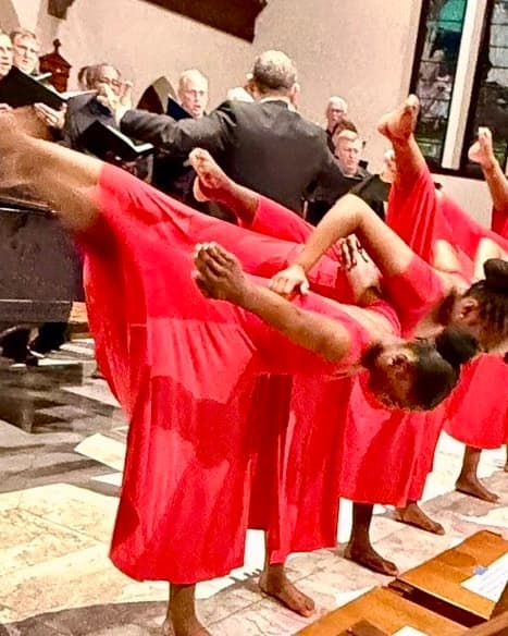 Three dancers in red mid-arabesque, the choir singing behind them.